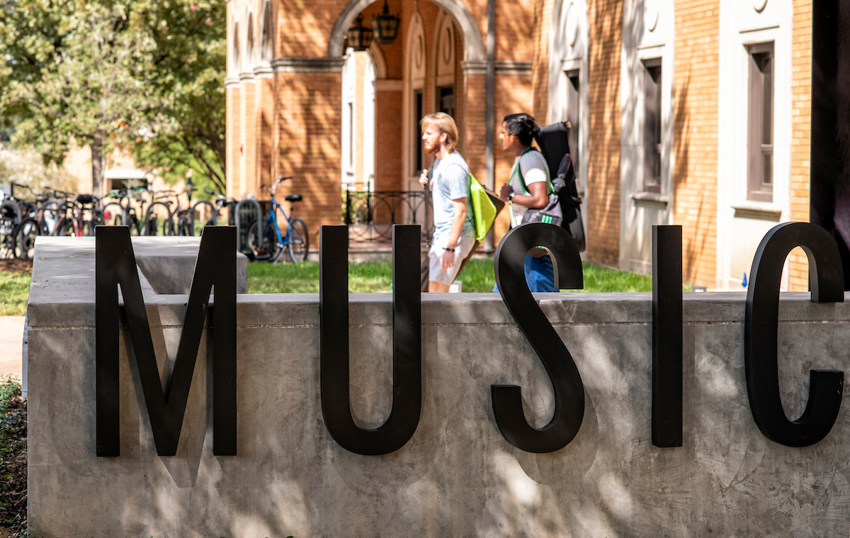 Students walking outside the music building behind a sign that says "MUSIC"