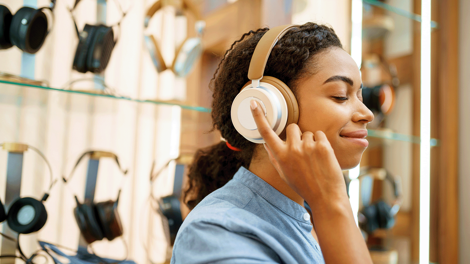 Girl listening to headphones in front of a wall display of headphones