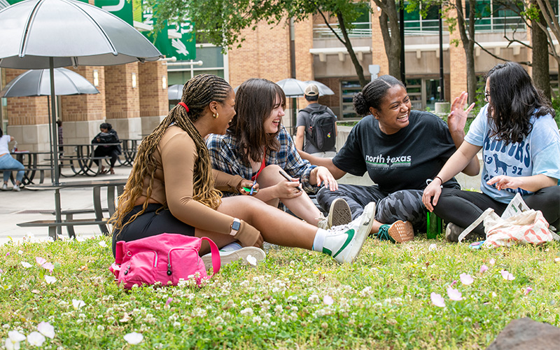 Four students sitting on a lawn at UNT. 