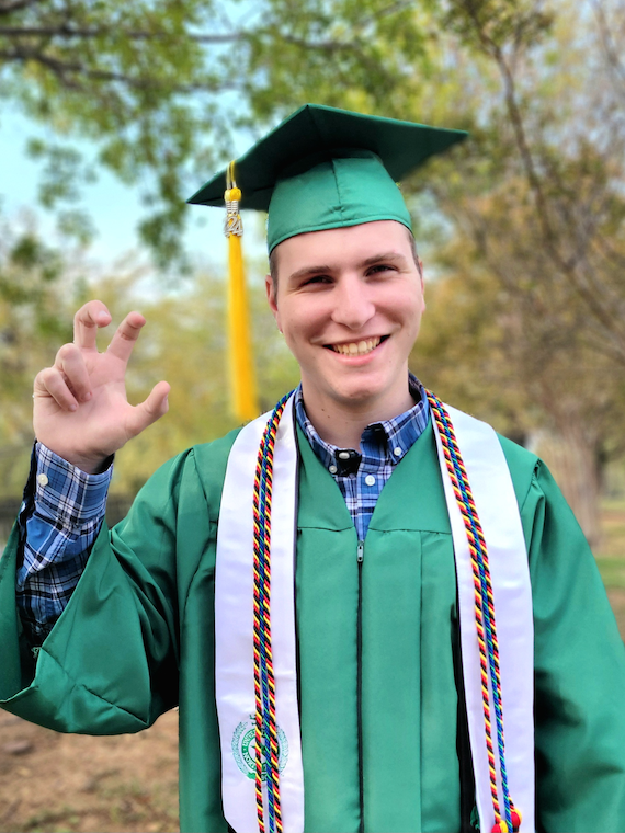 Scott Sennetti in commencement regalia, making the UNT eagle claw hand sign